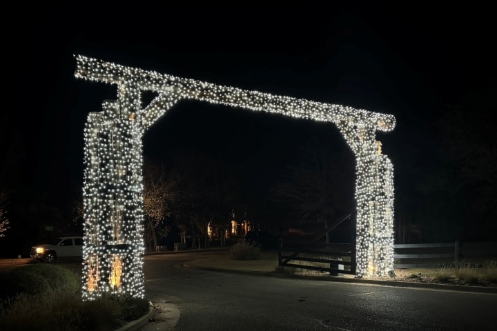 Entrance archway illuminated with white Christmas lights at night. The decorative lights create a festive, welcoming gateway, enhancing the rural landscape.
