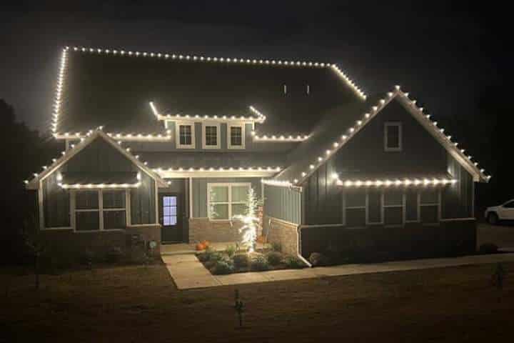 House illuminated with bright white Christmas lights outlining the roofline and windows, creating a festive holiday scene at night.